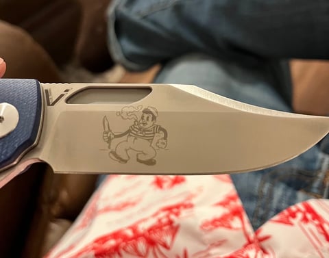 Close-up of a folding knife blade with an engraved cartoon pirate character design