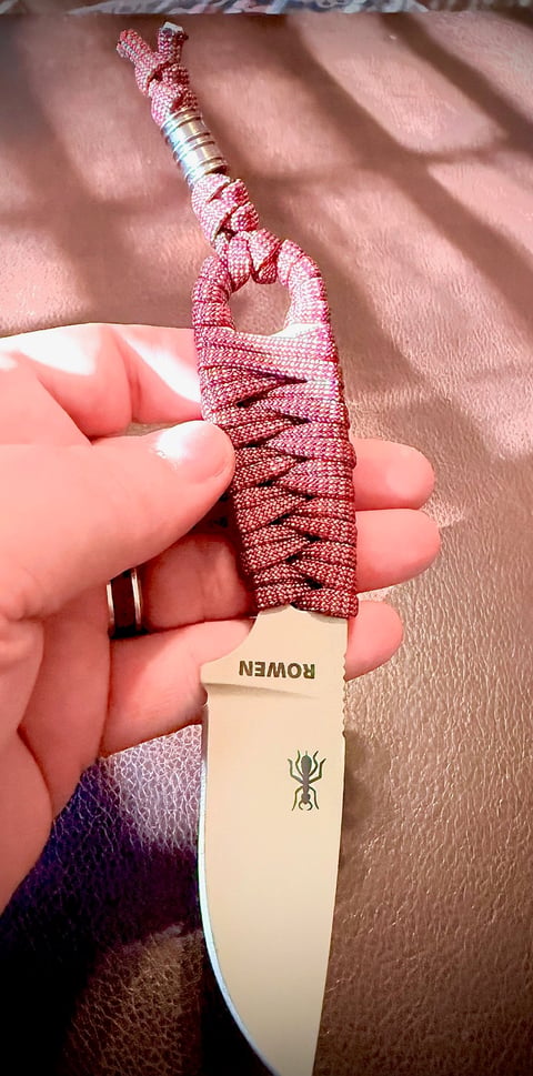 Person holding a small decorative knife with a red textured handle wrapped in cord and an ant emblem on the blade