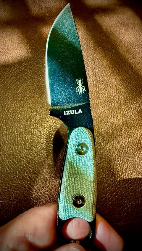 Izula fixed blade knife with green textured handle and metallic blade held in hand against brown leather background