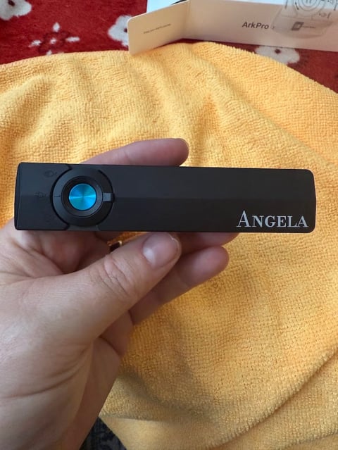 Hand holding black Angela brand portable projector with blue lens