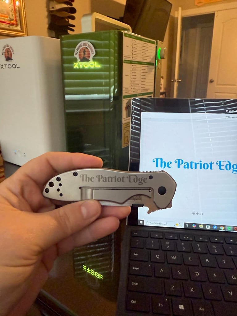 Person holding The Patriot Edge pocket knife with metal blade and white handle in kitchen with computer desk visible in background