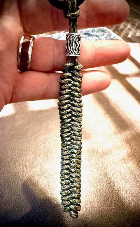 Hand holding a braided green and tan paracord with a decorative metal slider bead