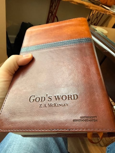 Hand holding a leather-bound Bible titled Gods Word by Z.A. McKinley with a turquoise ribbon bookmark