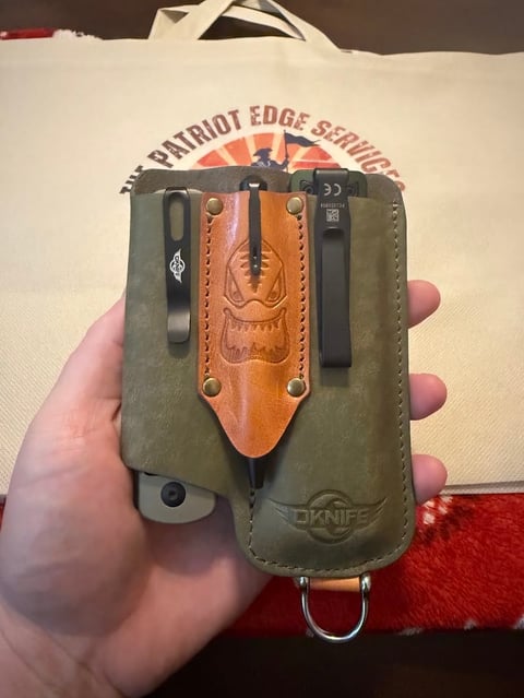 Hand holding a green and tan leather knife sheath with decorative tooling