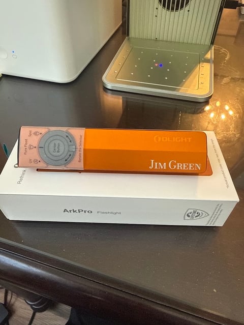 Orange flashlight labeled Jim Green sitting on ArkPro Flashlight box