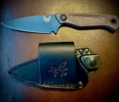 Benchmade fixed blade knife with blue steel blade and tan handle next to black leather sheath with embroidered logo