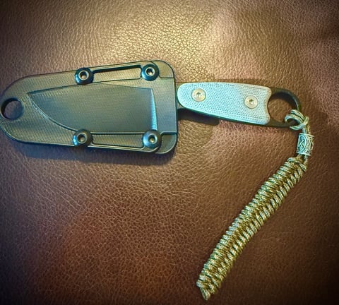 Fixed blade knife with teal handle and paracord lanyard on brown leather background