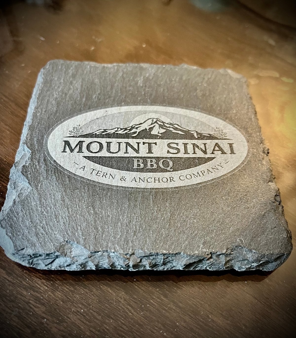 Square stone coaster engraved with Mount Sinai BBQ logo and Fern & Anchor Company text
