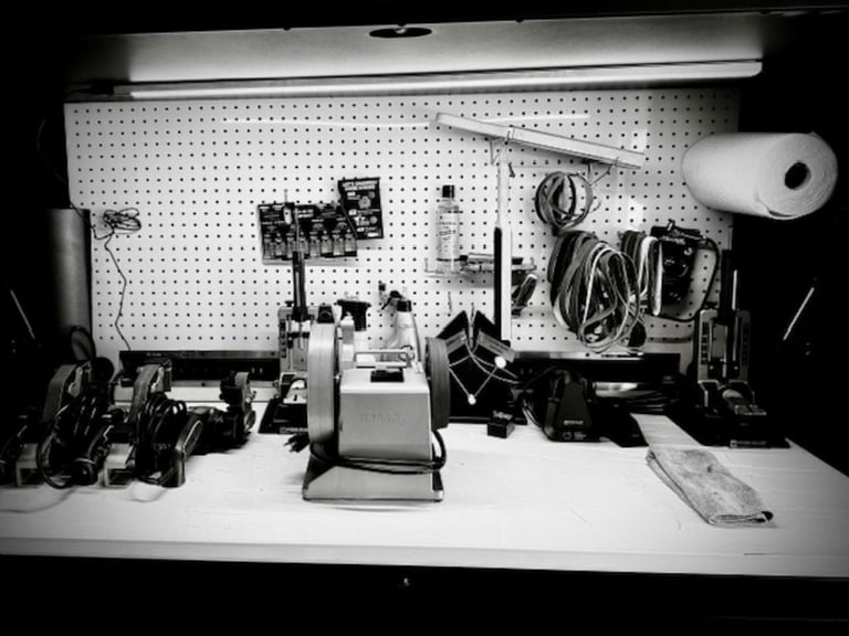 Organized workbench with pegboard wall storage, electronic equipment, cables, and tools arranged on white surface beneath fluorescent lighting