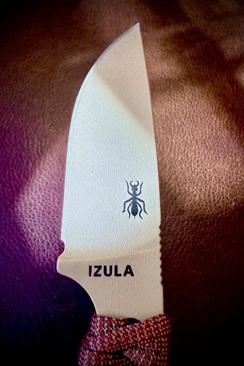 White IZULA knife with ant logo on blade, displayed against brown leather background